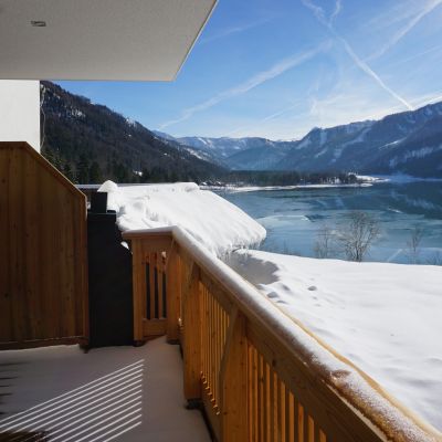 2020-Winter-Landhaus-Seereith-Faistenau-8 Blick vom überdachten Balkon mit Holzgeländer auf den zugefrorenen Hintersee und die verschneite Berglandschaft bei Sonnenschein
